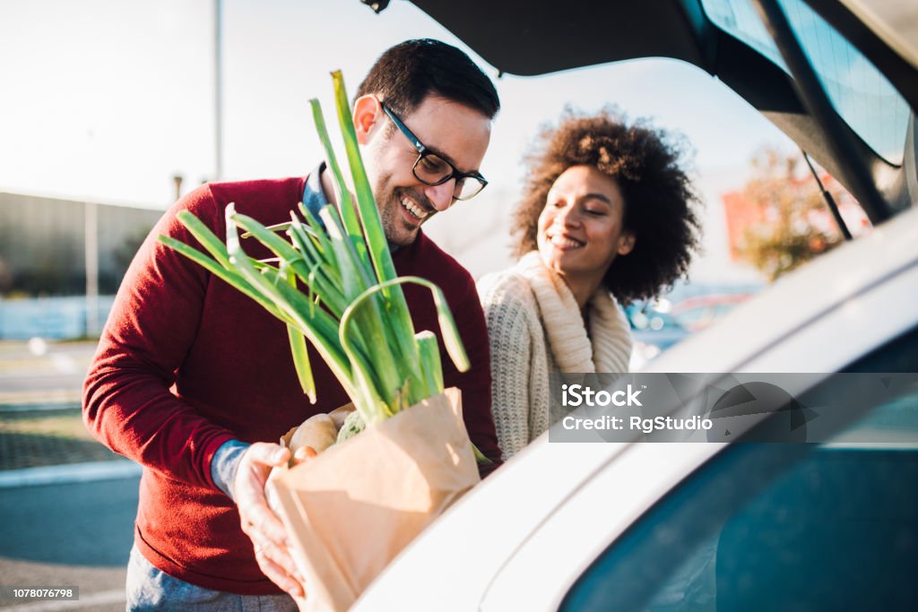 Man and woman putting groceries in the back of a car.